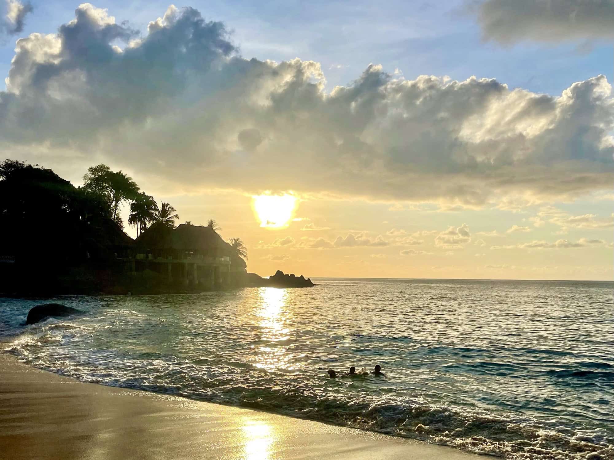 Sunset sur une plage de Mahé, Seychelles, avec des cocotiers, des eaux turquoise et un ciel nuageux coloré.